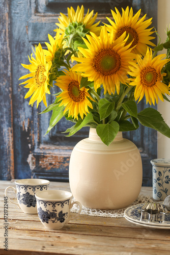 Girasoli su vaso di ceramica sopra un tavolo di legno con alcuni oggetti da cucina sparsi