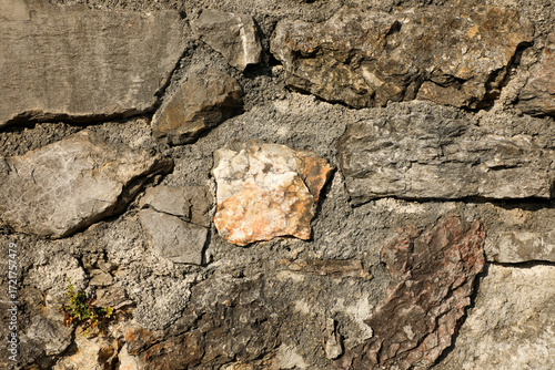 Rough stone wall built with irregular rocks and gray concrete mortar, ideal for backgrounds that emphasize natural texture and rugged design.