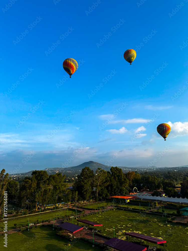 Obraz premium Vibrant and colorful hot air balloons flying over a scenic road and green countryside landscape in Mexico on a beautiful clear day.