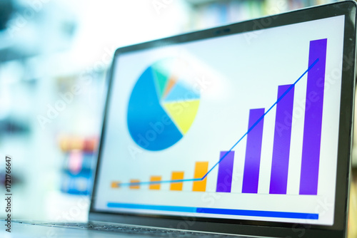 A laptop screen displaying a graph and a book placed on the table in the library, representing a business concept.	