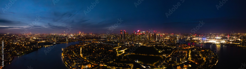 Naklejka premium Panorama of London skyline at night showcases vibrant city lights and the Thames River, aerial drone shot.
