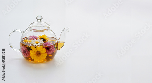 Glass teapot with floral tea and yellow daisies on white background  