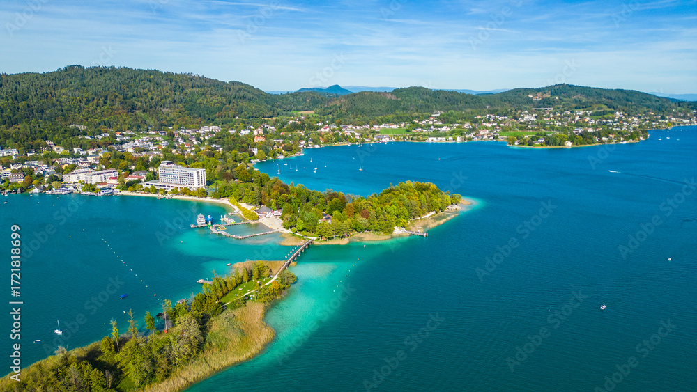 Fototapeta premium Aerial view of Portschach am Worthersee, Austria, with turquoise lake waters, boats, piers and alpine scenery. Popular summer holiday destination for relaxation, wellness and tourism