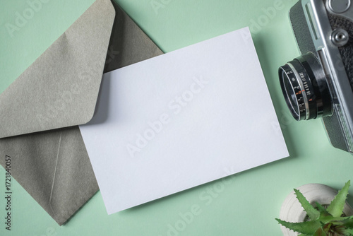 Empty white blank greeting or invitation card, envelope, vintage camera, cactus on green background.