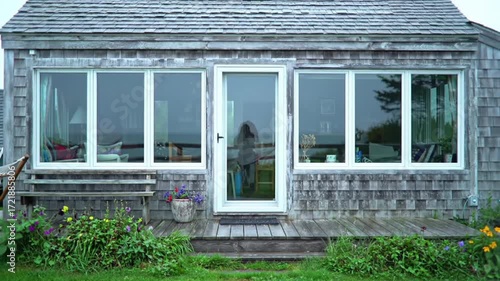 Seaside cottage facade with large windows showcasing a tranquil ocean view.