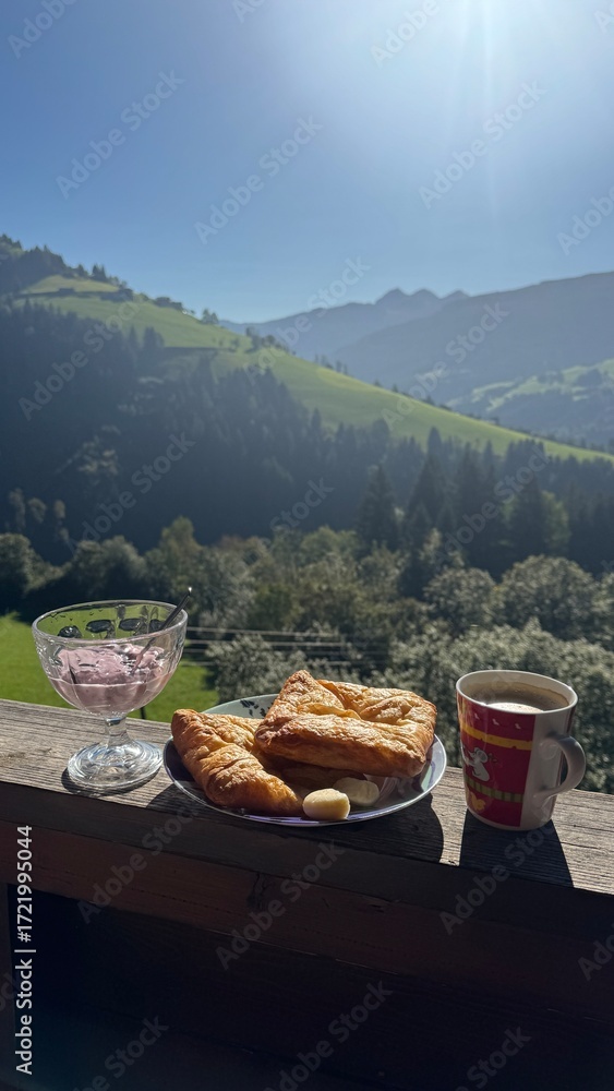 Fototapeta premium Scenic mountain breakfast with croissants, cheese, coffee, and yogurt in a glass bowl, set against a backdrop of sunlit alpine hills and forest in the early morning light.