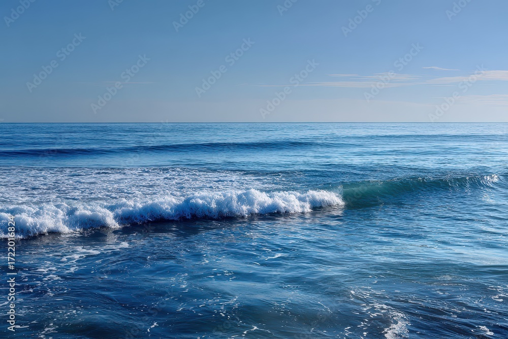 Fototapeta premium Gentle ocean waves lapping on tranquil deep blue water under clear sky at midday, creating a serene coastal ambiance and inviting relaxation