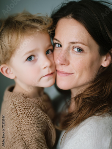 Close-up portrait of a loving middle-aged mother holding her young son cheek to cheek, both smiling and looking at the camera, capturing a warm, affectionate family moment