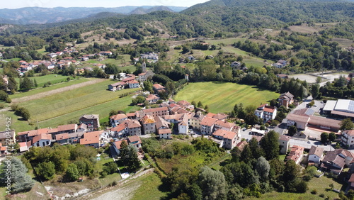 Wallpaper Mural Aerial view of Battaglia, Mioglia, Italy, showcasing a charming Italian village with red-tiled roofs nestled amidst vibrant green fields and rolling forested hills under a clear September sky. Torontodigital.ca