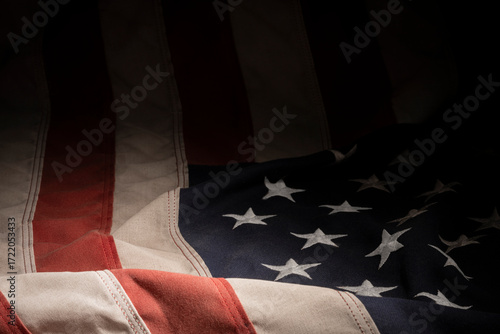 faded old American flag fades off into shadow with the blue field of white stars in the foreground.