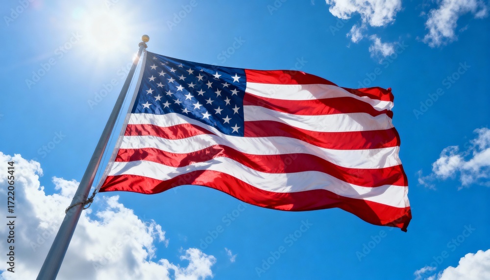 Fototapeta premium Low-angle view of large US flag waving under bright sky, emphasizing patriotism and grandeur