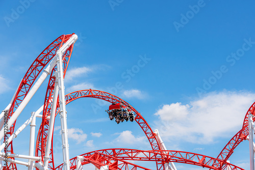 Roller coaster in Prater Vienna summer sky, thrilling red loops and riders enjoying amusement park adventure in vibrant season atmosphere.