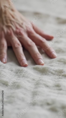 Extreme close-up video of an unblemished hand gently gliding and pressing pristine organic linen, creating ripples, highlighting texture under soft natural light. Concept of natural well-being