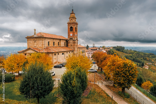 Old parish church stands among colorful autumnal trees in Diano d'Alba, Italy.