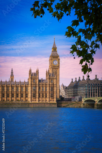 Big Ben, Westminster Abbey, and the bridge at sunset in London, framed by sycamore branches over the River Thames, a timeless tranquil cityscape of the United Kingdom