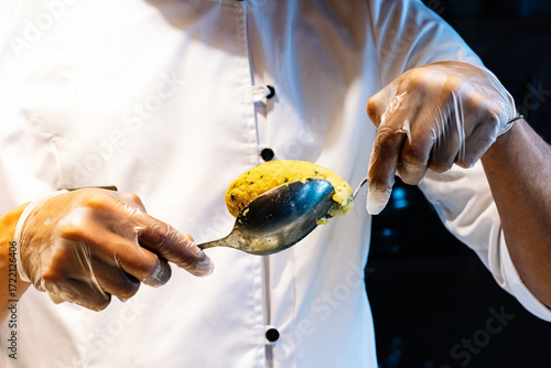 The chef's gloved hands meticulously form a delicious cod croquette using serving spoons, demonstrating the creation of a culinary specialty in Porto, Portugal.