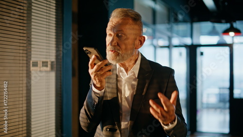 Valokuva Executive dictating audio notes on smartphone walking corridor sunset closeup