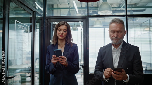 Successful businesspeople walking hallway looking cellphones closeup. Partners