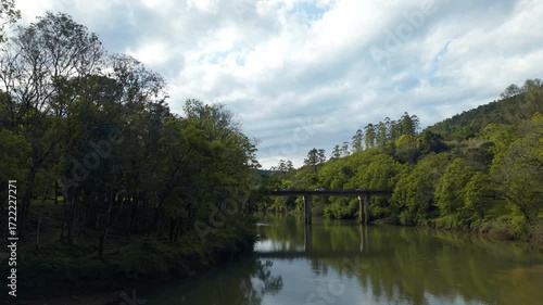 Bridge over green river flowing amid trees and rocks. Irani river. 4K. Aerial. Drone.