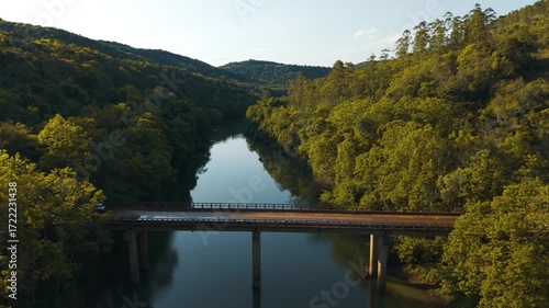 Cars passing over a bridge. Green river amid trees on a sunny day. Irani river. 4K. Aerial. Drone.