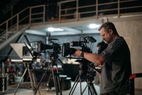 The director of photography with a camera on the set. A professional videographer is working on filming a movie or commercial for a TV series. The filming process takes place indoors in a studio.