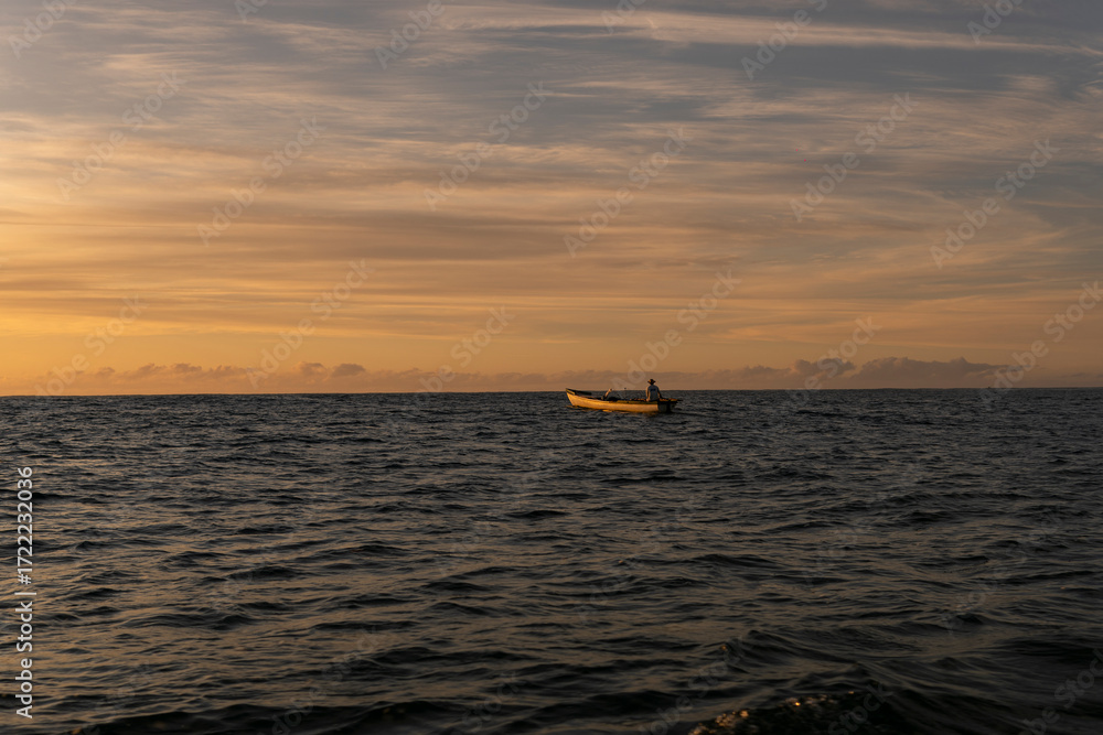Fototapeta premium Golden sunrise in Itacaré, Bahia, Brazil. Boats floating on calm sea, yellow light on the horizon, tropical coastal landscape with warm tones and natural beauty.
