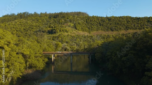 Cars passing over a bridge. Green river amid trees on a sunny day. Blue sky. Irani river. 4K. Aerial. Drone.