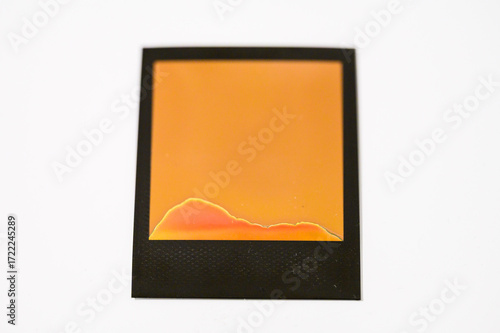 Failed instant film development — abstract orange and red chemical marks on blank Polaroid photo frame on white background