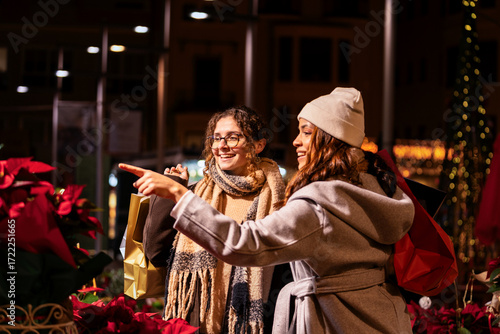 Two smiling women shopping for poinsettias at a festive outdoor christmas market