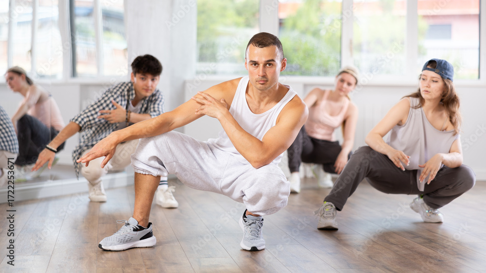 Fototapeta premium Active young guy performing seated pose of breakdance in training hall during dancing classes