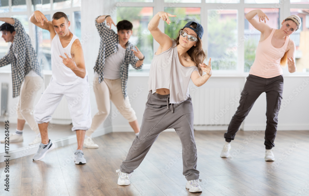 Fototapeta premium Young girl standing performs basic hip hop movements in front of group of students. Developing precise movements, rehearsing arc elements, nae nae moving