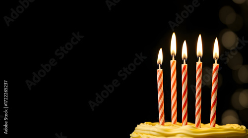 Burning birthday candles on a dark background cast a yellow glow of light over a celebration cake