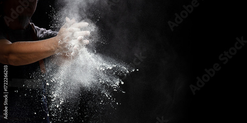 Chef prepare white flour dust for cooking bakery food. Elderly man Chef clap hand, white flour dust explode fly in air. Flour stop motion in air with freeze high speed shutter, black background