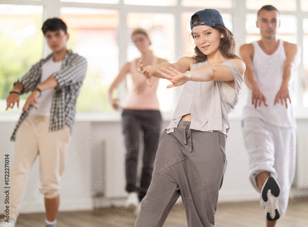 Naklejka premium Young girl standing performs basic hip hop movements in front of group of students. Developing precise movements, rehearsing arc elements, nae nae moving