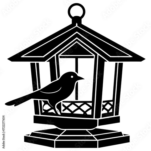 Black silhouette of a bird perched on a traditional wooden bird feeder with a hanging loop