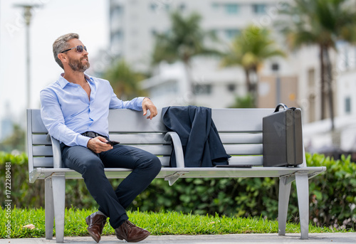 Businessman relax on bench with briefcase outdoor. Businessman in suit. Mature Hispanic businessman. Business boss with briefcase. Business man. Successful business. Copy space