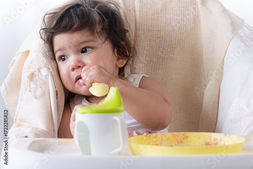 Innocence toddler kid sloppy mouth hand eating birthday cake sitting on chair at home. Happy mixed race children daughter with sweet birthday cake messy face enjoyment sitting chair. Growing life.