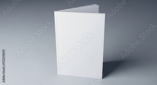 A blank, white, folded card stands upright on a smooth, grey surface, casting a shadow.