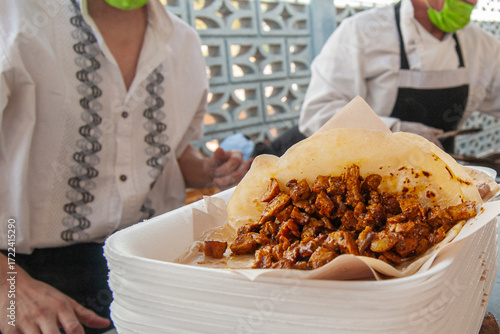 Preparation of charcoal-grilled beef tacos in a flour tortilla on a disposable plate at a staff meeting in Mexico, with cooks in the background