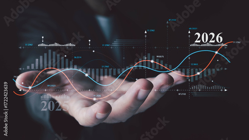 A person's hand presents a futuristic holographic chart showing financial growth predictions for 2026. Data includes bar graphs, trend lines, and fluctuating numbers on a dark background.