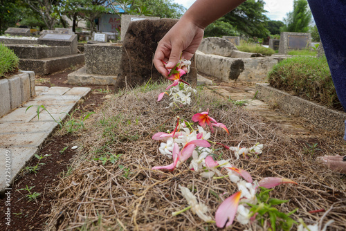 a man placing tropical flowers on an Indonesian grave, showing respect