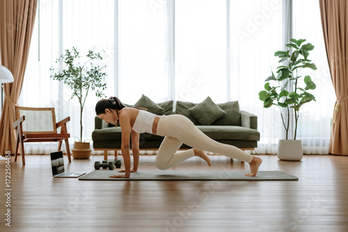Young Asian woman doing sport exercises indoor. Beautiful girl workout at home. Athletic outfit is doing mountain climber exercises