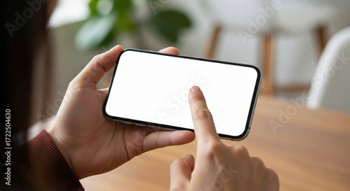 Close up of person holding a smartphone horizontally with finger touching blank screen for website or app interface mockup