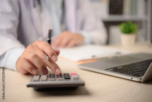 Doctor calculates medical billing at office desk with calculator laptop paperwork for insurance claim cost control finance management healthcare administration concept