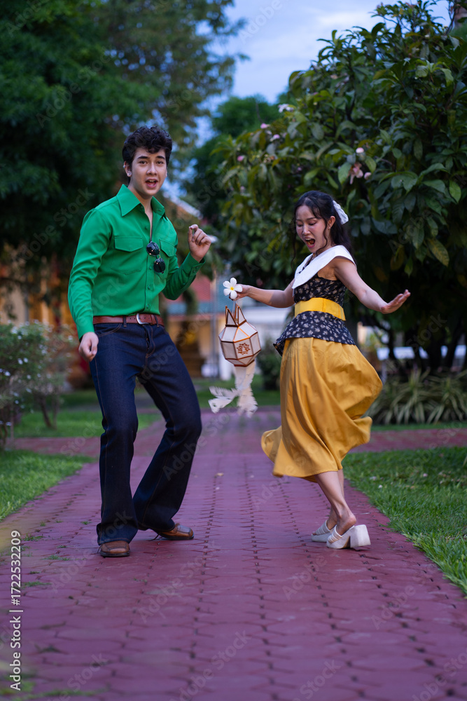 Obraz premium A young couple dressed in colorful retro-style outfits dancing together on a red brick walkway in a garden.
