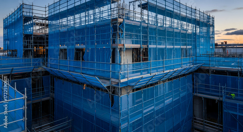 Modern building construction progress with blue safety netting at dusk