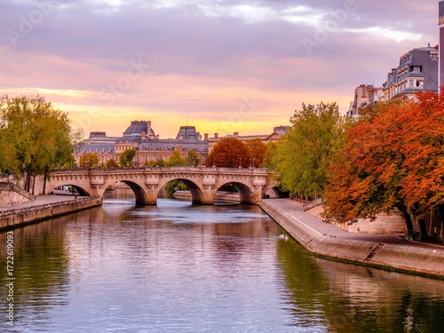 Pont Neuf over the Seine River with autumn foliage and historic Parisian architecture at sunrise in Paris, France.