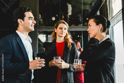 Three professionals in formal attire network at corporate reception, chatting with drinks. Event scene includes sales, partnership, seminar vibes, collaboration, planning, and new opportunities.