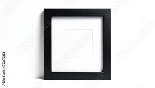 Black picture frame with white matte border, resting on a white surface, casting a soft shadow against a white wall, minimalist aesthetic