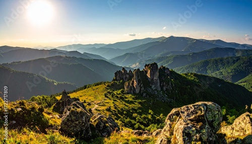 Majestic landscape with sunlit grassy mountains, striking rock formations, and hazy mountain ranges stretching toward the horizon under a clear sky
